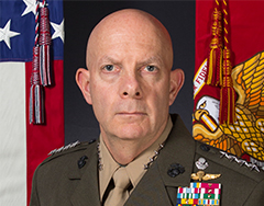Image of General David H. Berger; a man in military uniform stands in front of the American flag and Marine Corps flag. He has a number of insignia and badges on his suit. He is looking towards the viewer with a closed mouth.  