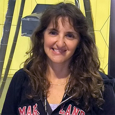 Sandra Irish is wearing a "Maryland" sweatshirt jacket, has curly brown hair, and is smiling showing her teeth.